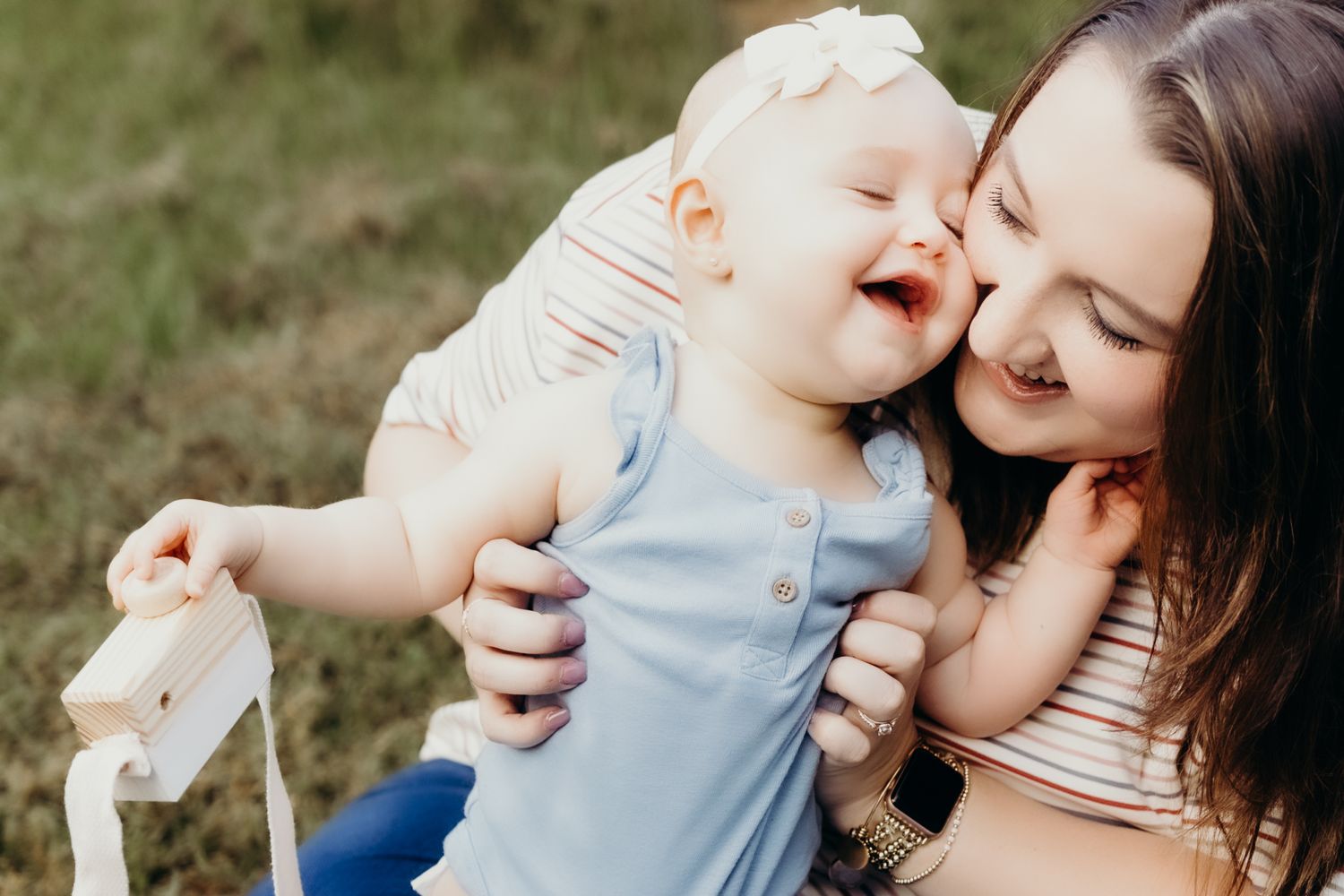 Tender outdoor family moment captured in natural sunlight on grassy field.