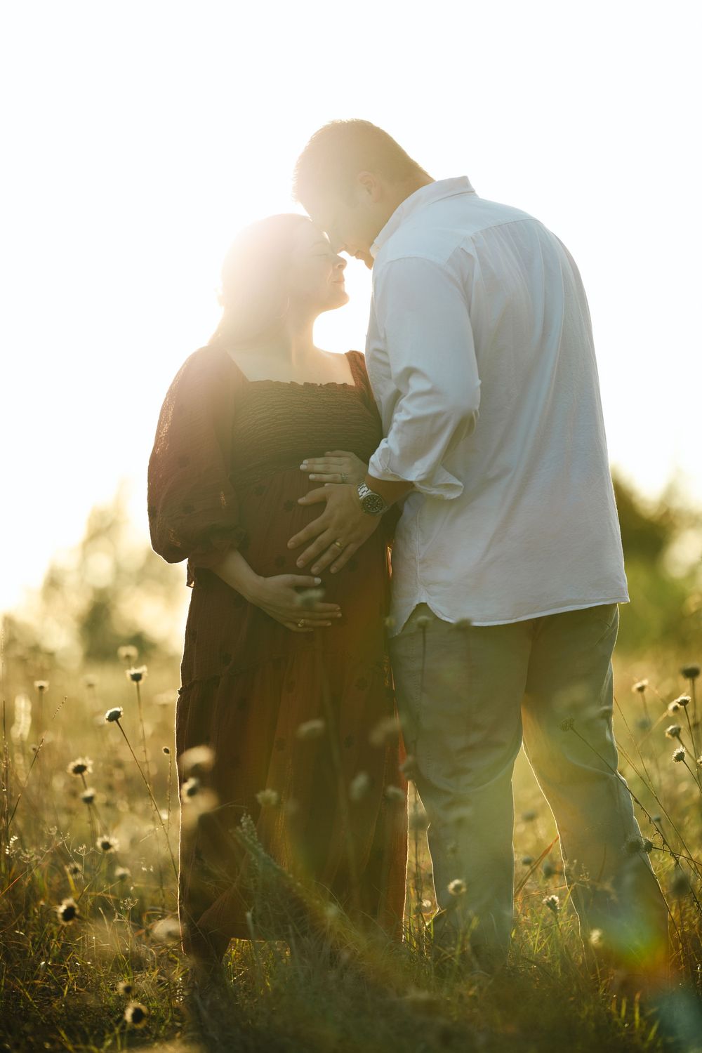 Silhouetted couple embraces in a sunlit meadow of dandelions during golden hour.