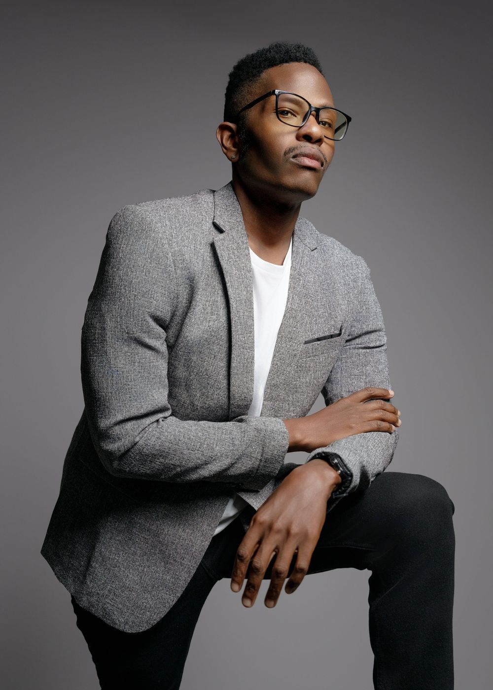 Professional studio portrait of a person in a gray blazer and white t-shirt against a gray background.