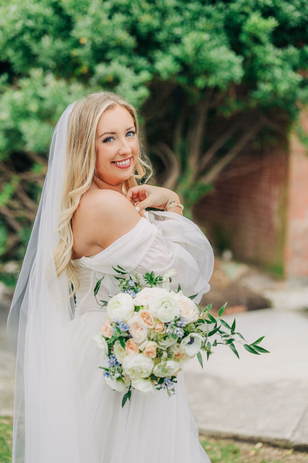 A bride in a flowing white dress twirls joyfully while holding a pastel bouquet of flowers in an outdoor garden setting.