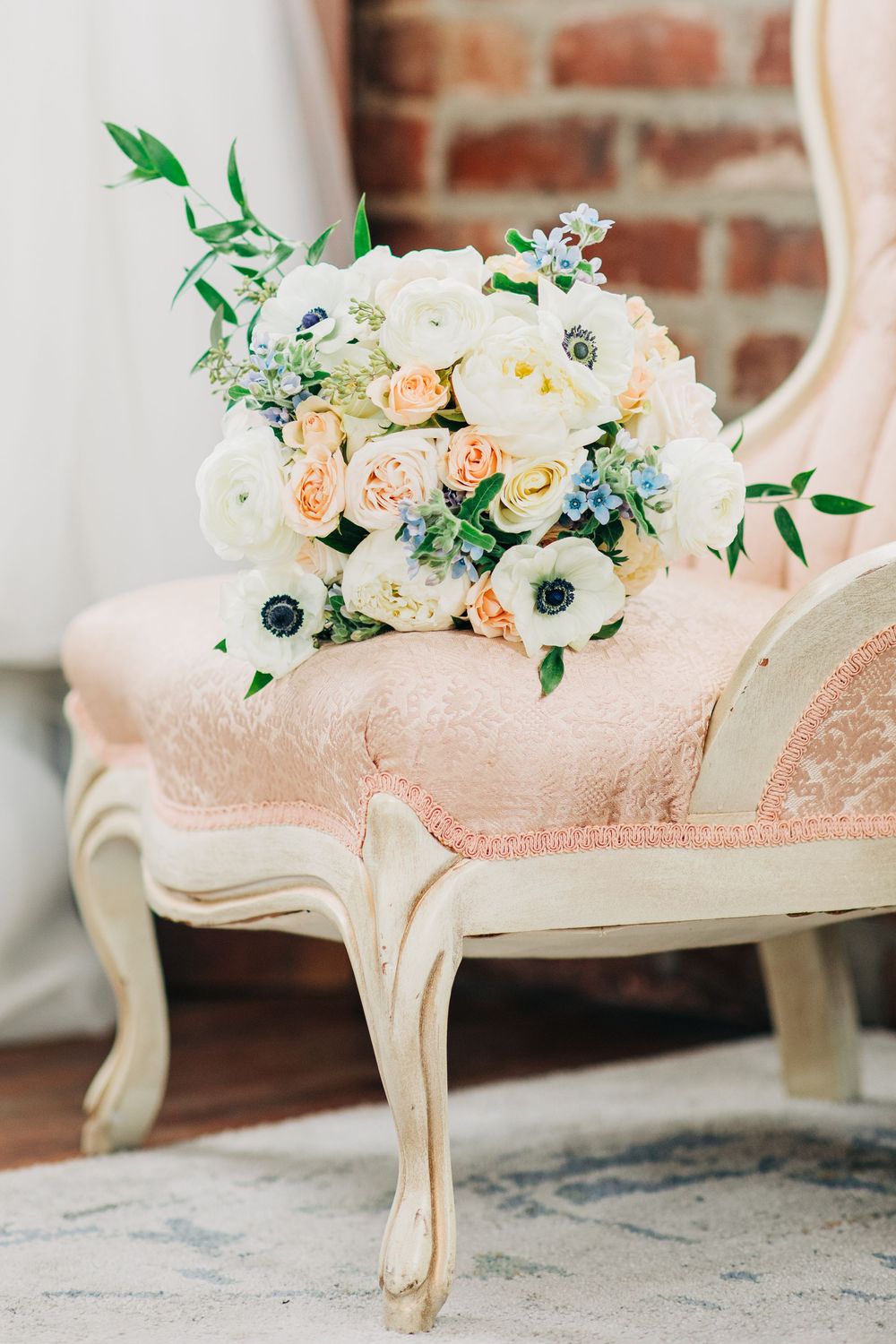 Elegant pink upholstered chair with curved legs decorated with a lush floral arrangement of white and peach blooms.
