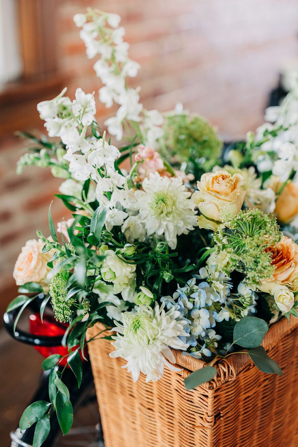 Fresh floral arrangements featuring white and peach blooms with greenery displayed in wicker baskets on wooden surfaces.