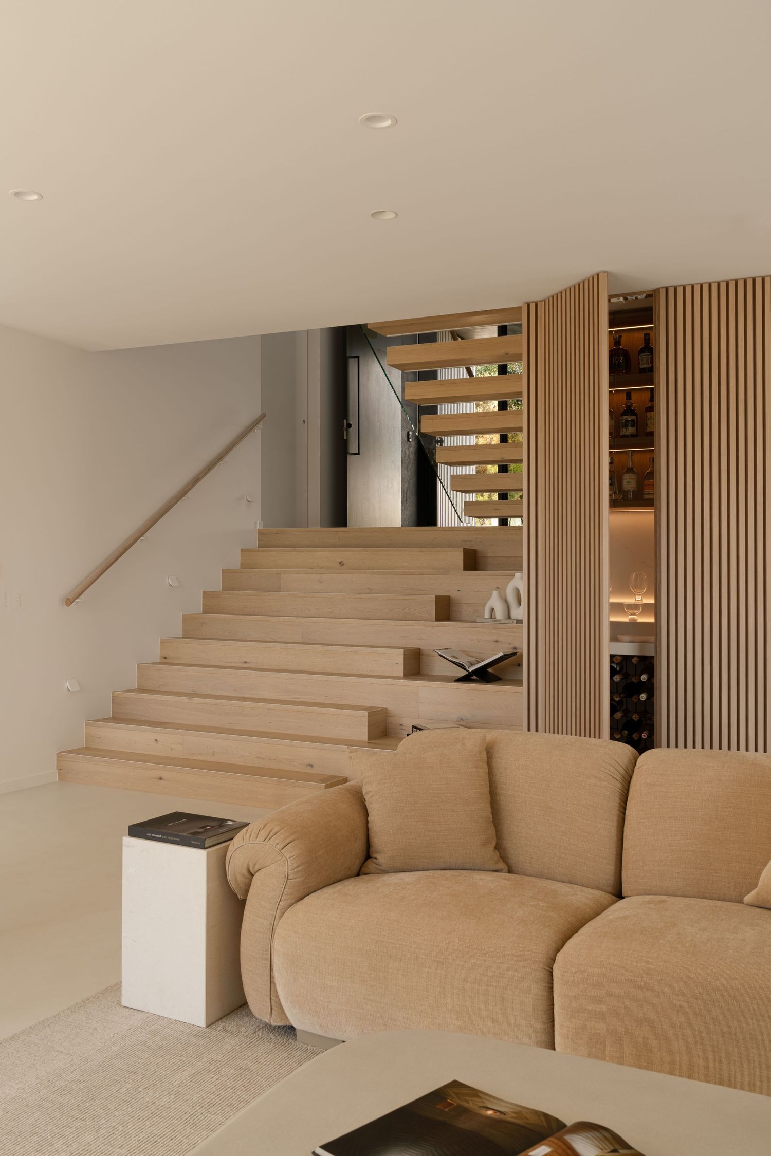 Contemporary living space with beige sectional sofa and wooden staircase featuring built-in storage.