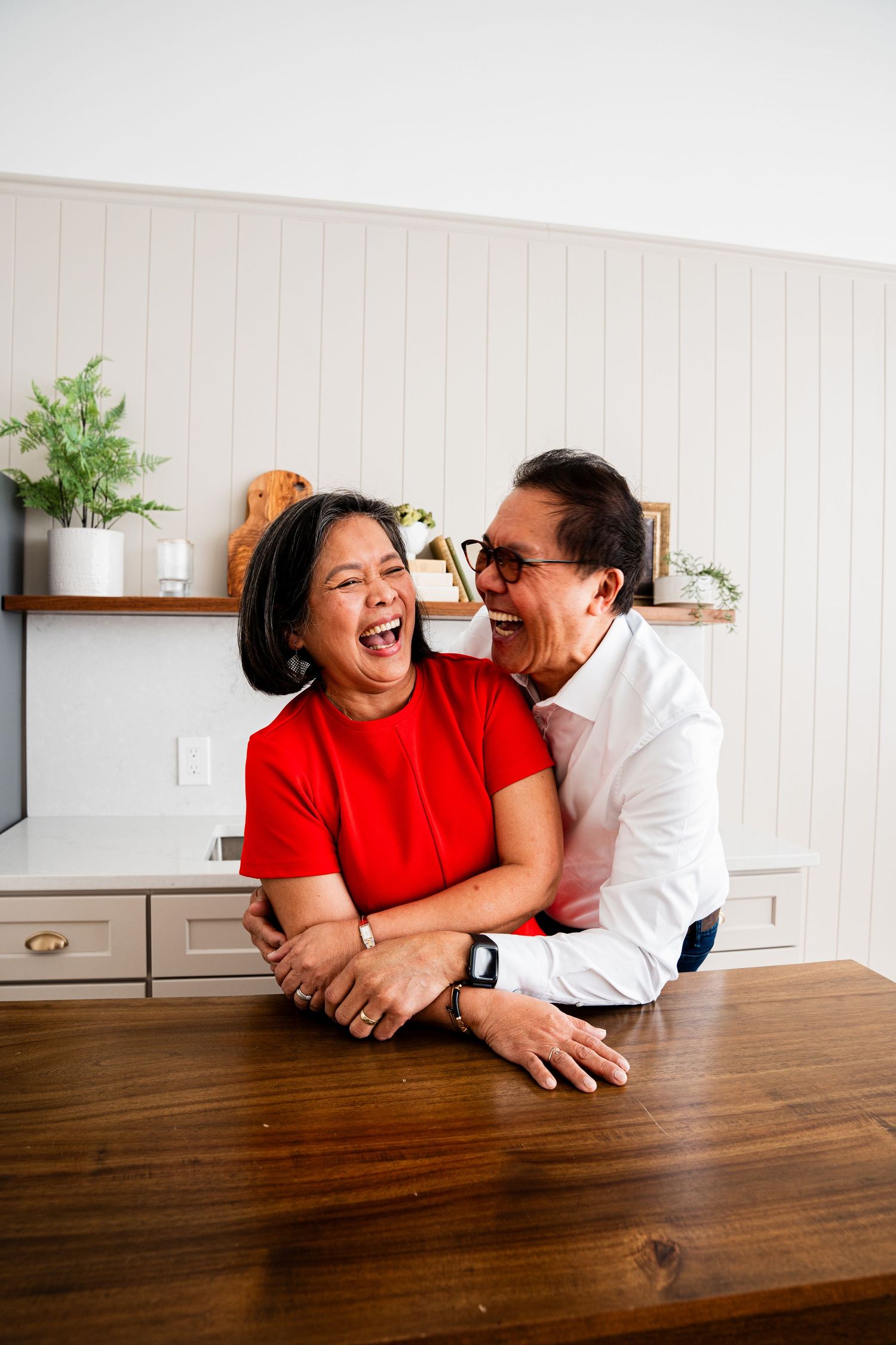 Couple laughing together while leaning on a wooden table in a bright kitchen interior.