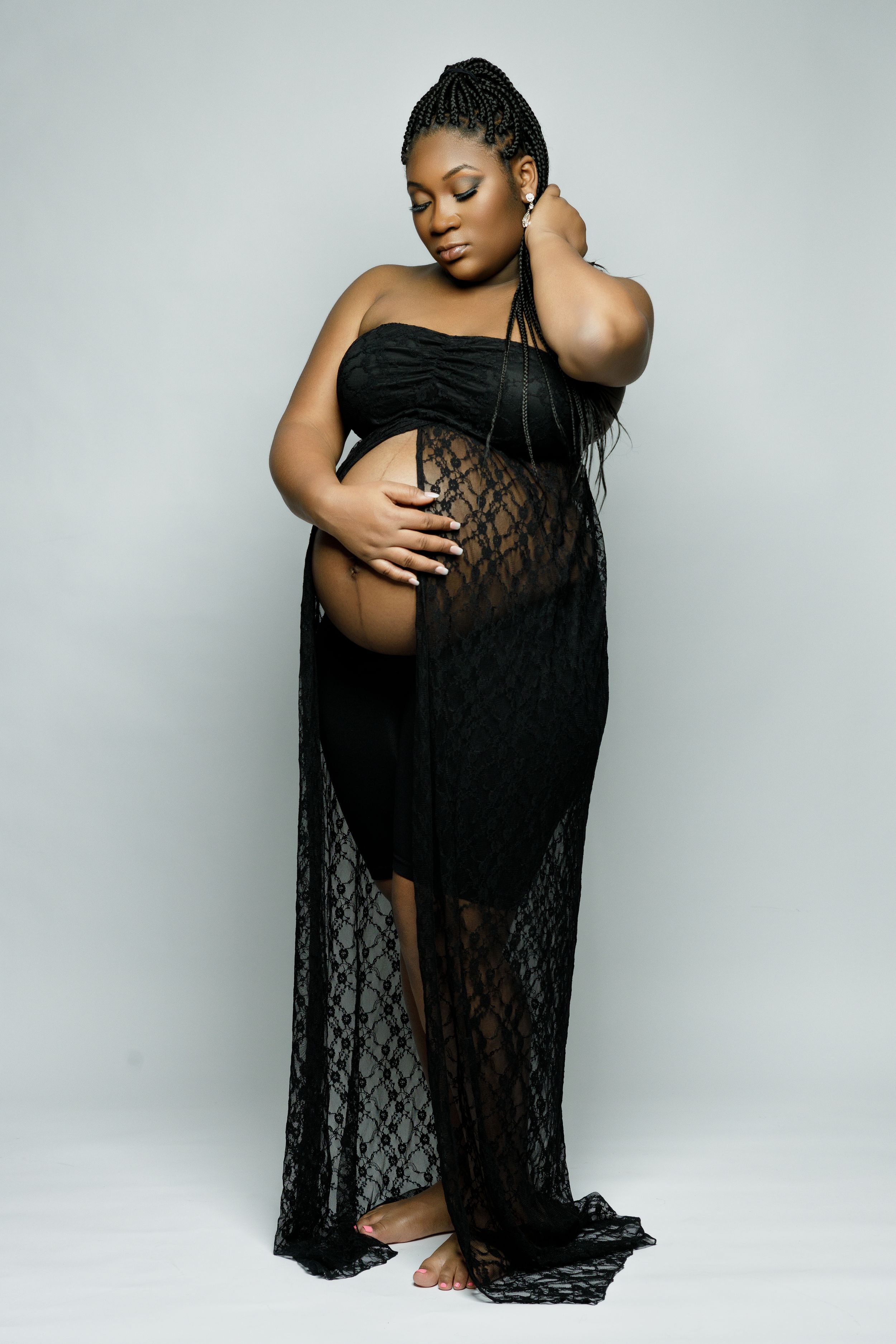 Artistic maternity photoshoot featuring elegant black lace dress against light background.