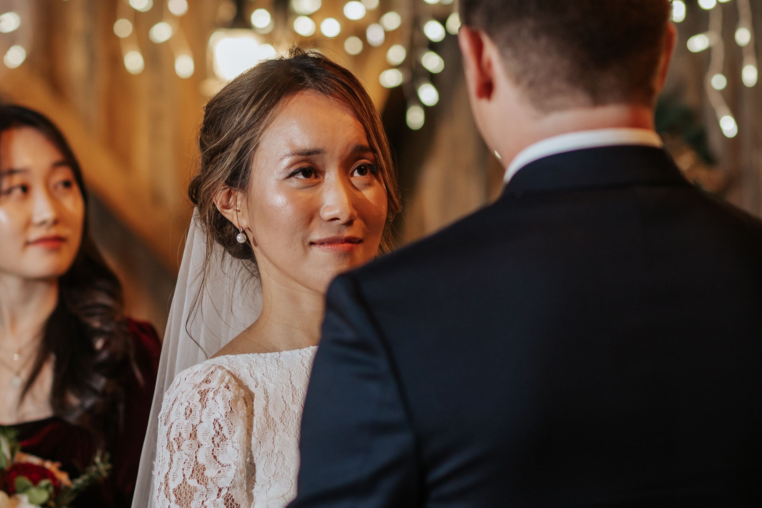 A bride and groom share an intimate moment during their wedding ceremony under twinkling lights and decor.