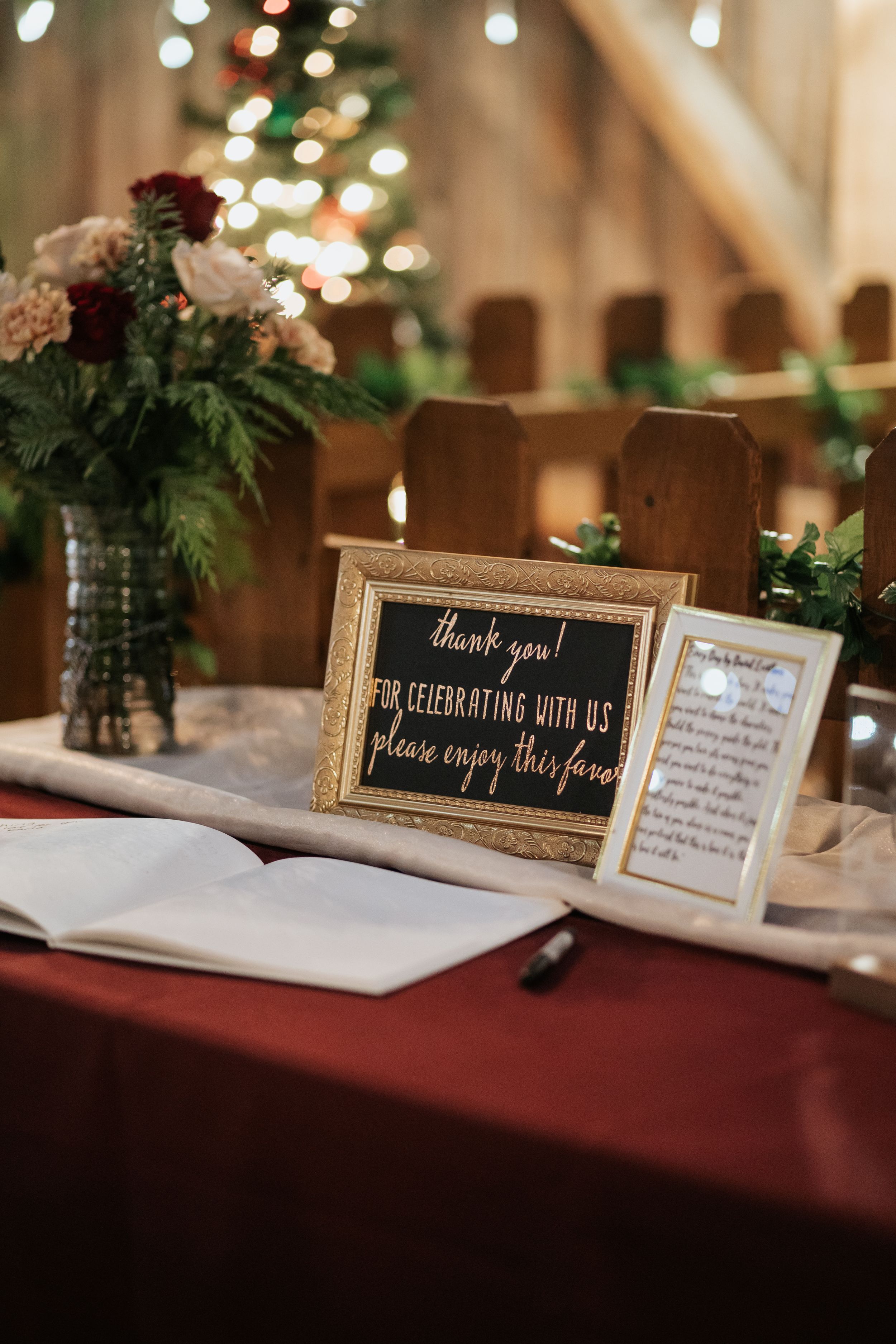 Vintage-framed welcome signs and guest messages displayed on burgundy tablecloth at rustic wedding reception.