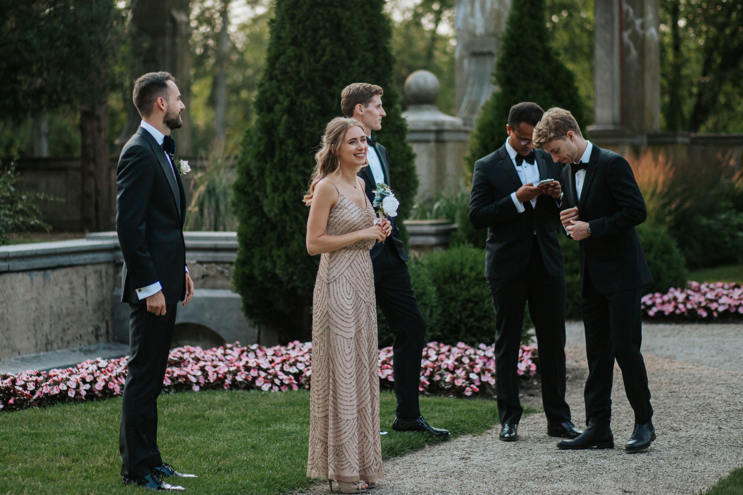 Wedding party gathers for intimate outdoor ceremony in a lush garden setting with blooming pink flowers.