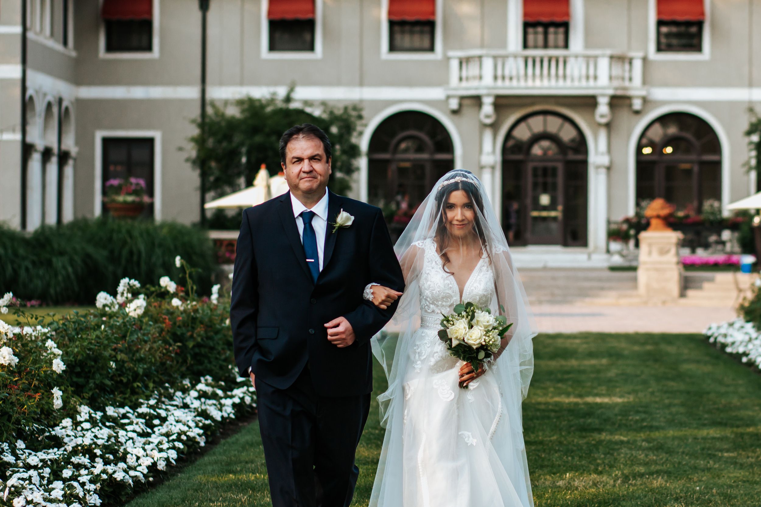 A happy couple walks together during their wedding celebration at an elegant outdoor venue with white floral decorations.