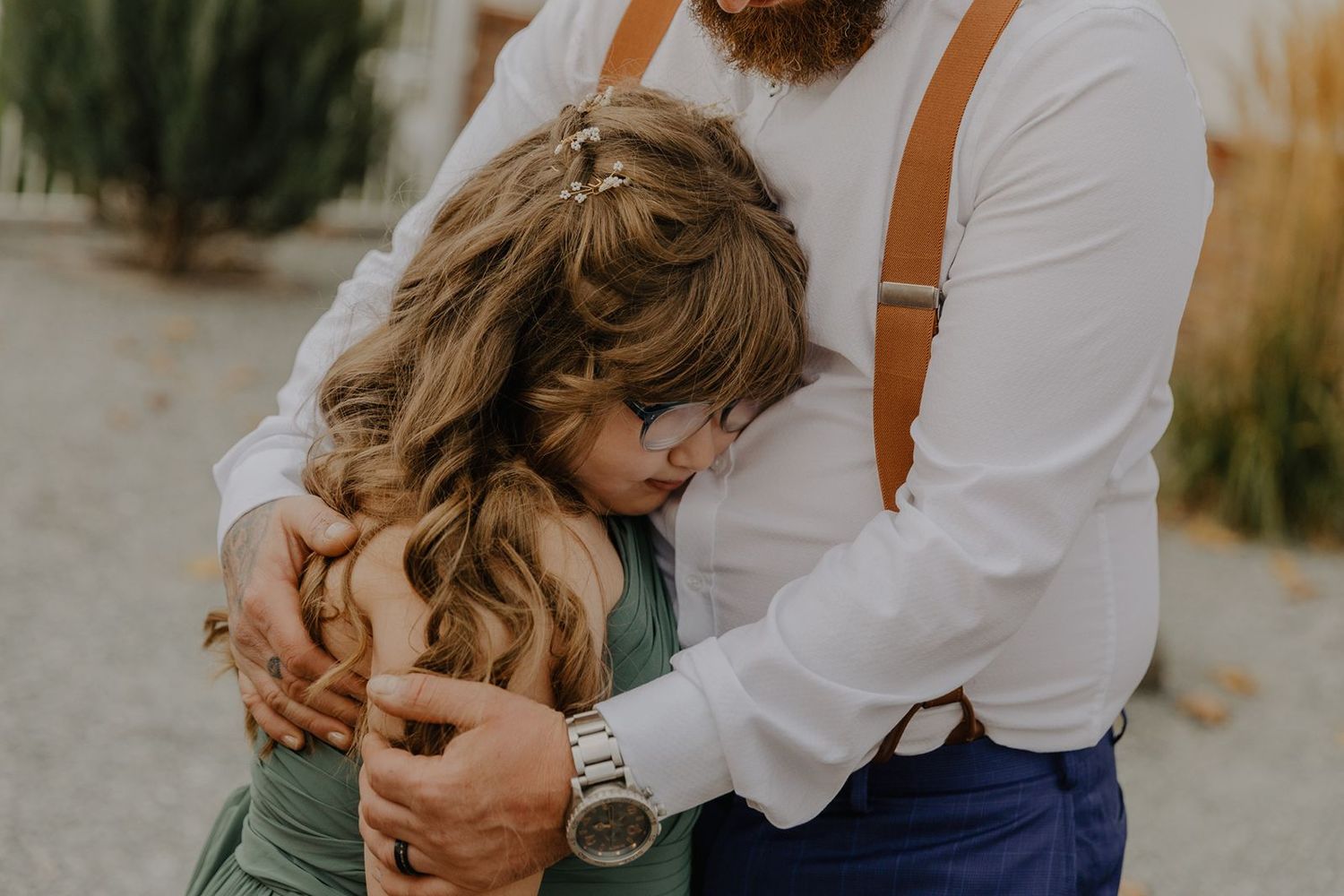 A bride and groom share a tender group hug outdoors during their wedding day.