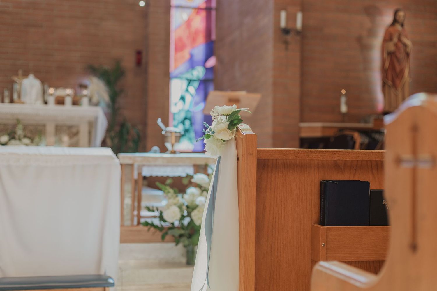Church pew decorated with white floral bouquet for wedding ceremony with altar in background.
