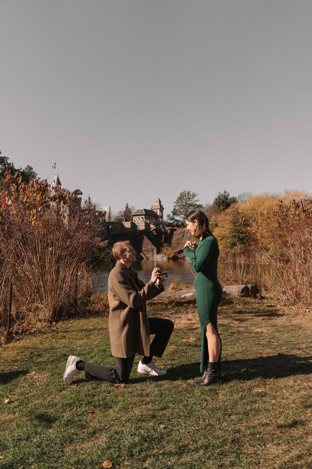 Two people share a romantic moment during a proposal on a grassy hillside in autumn.