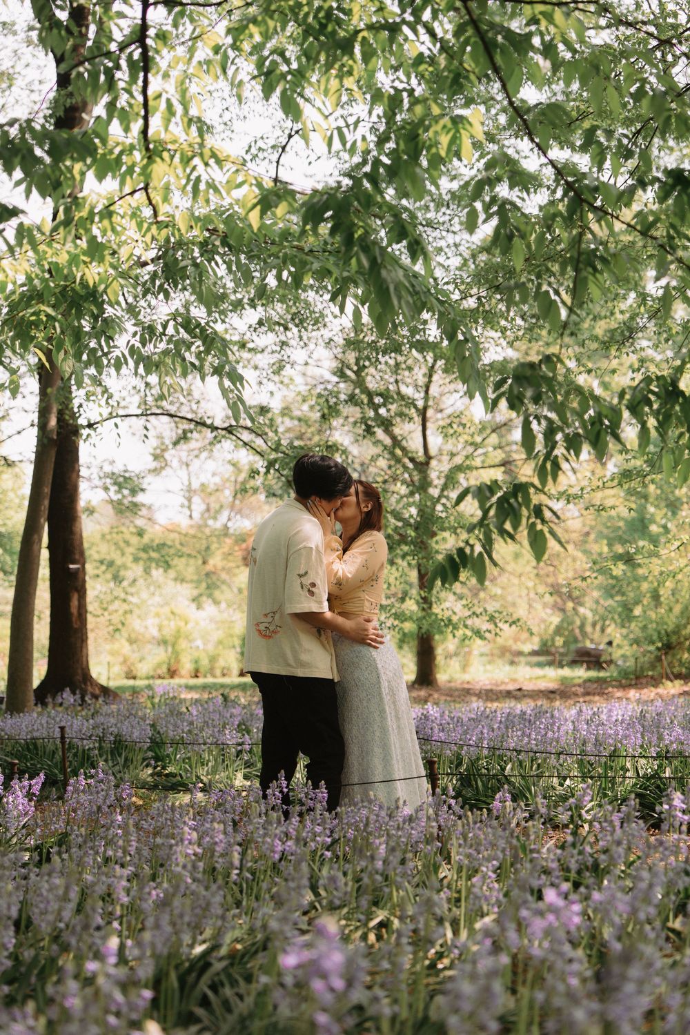 Romantic moment in field of purple wildflowers with trees in background.