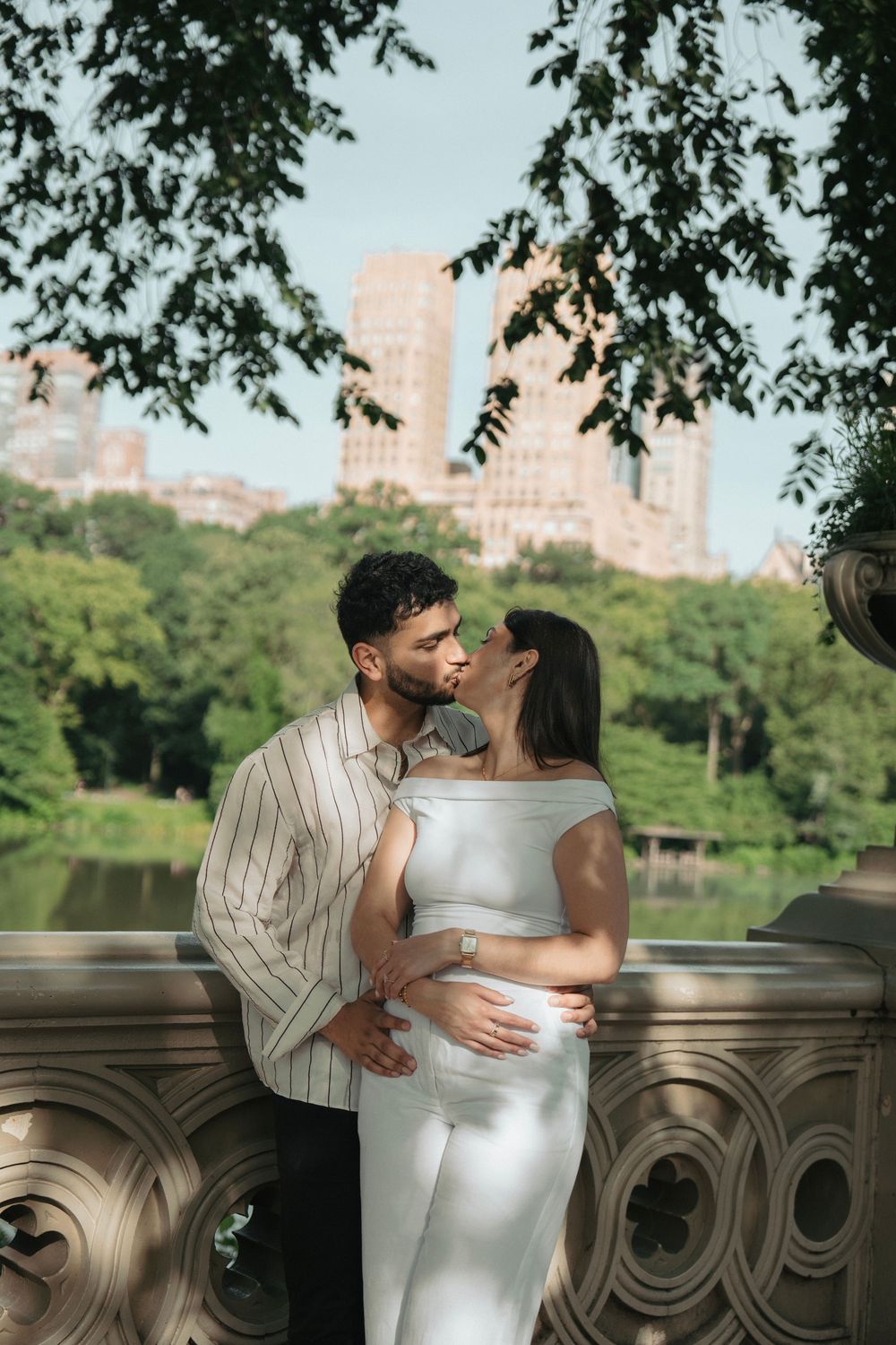 A couple sharing an intimate moment on a stone balcony in Central Park with trees in the background.