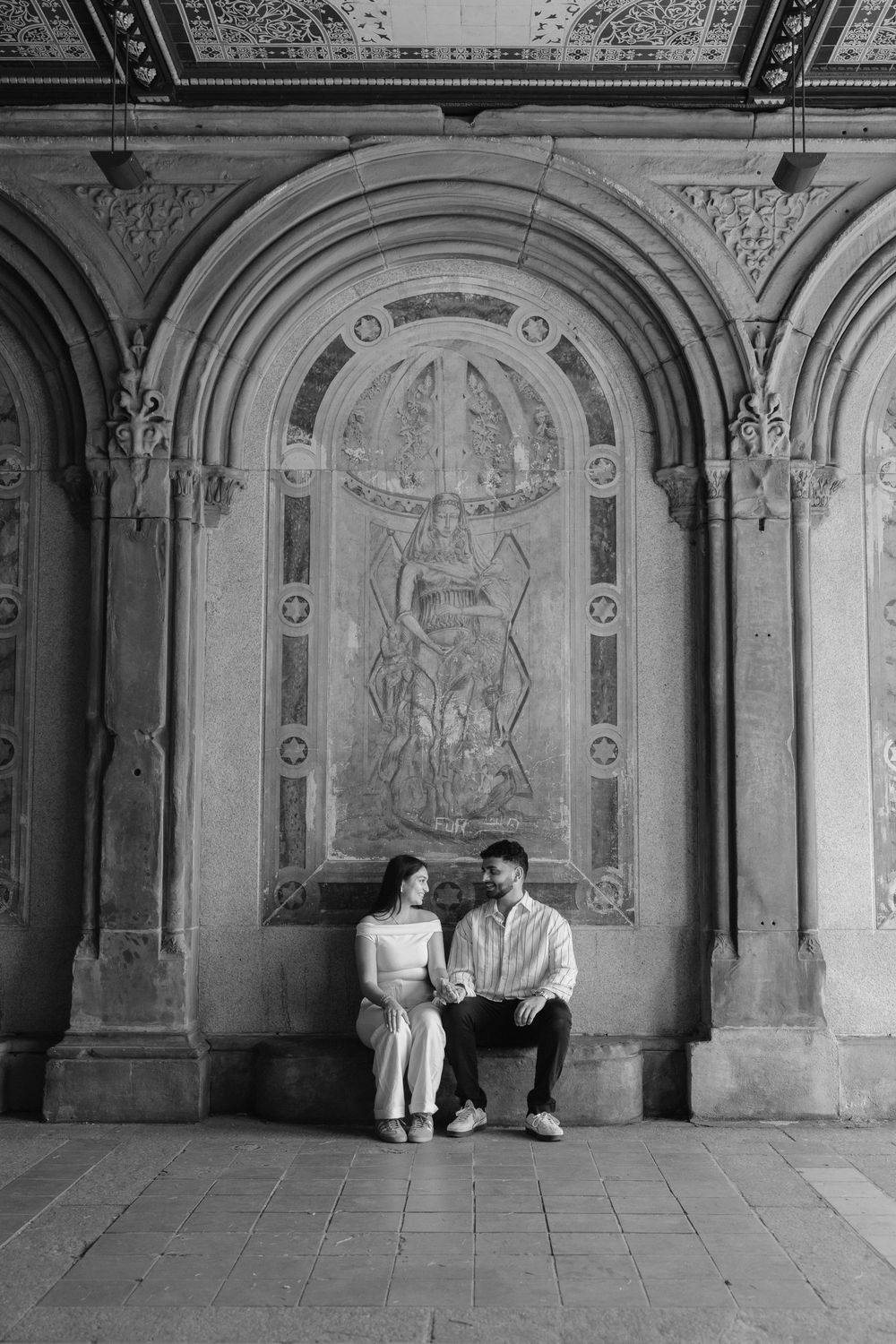 A couple posing in an ornate archway with decorative wall murals.