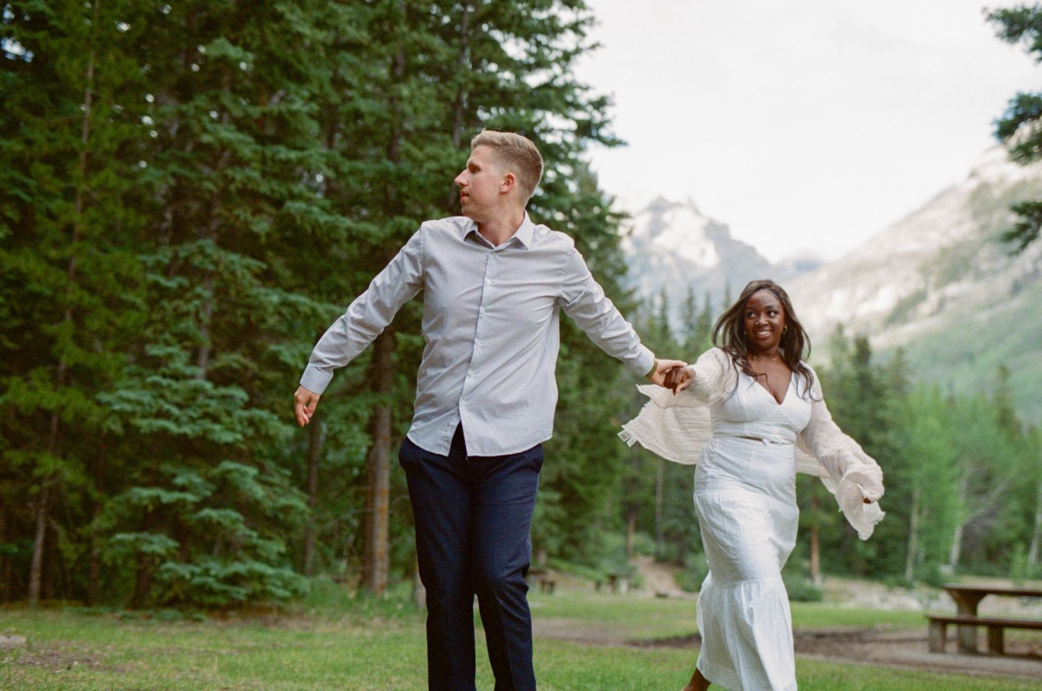 35 mm film photo of bride and groom holding hands and spinning around in a lush green campground in Banff National Park