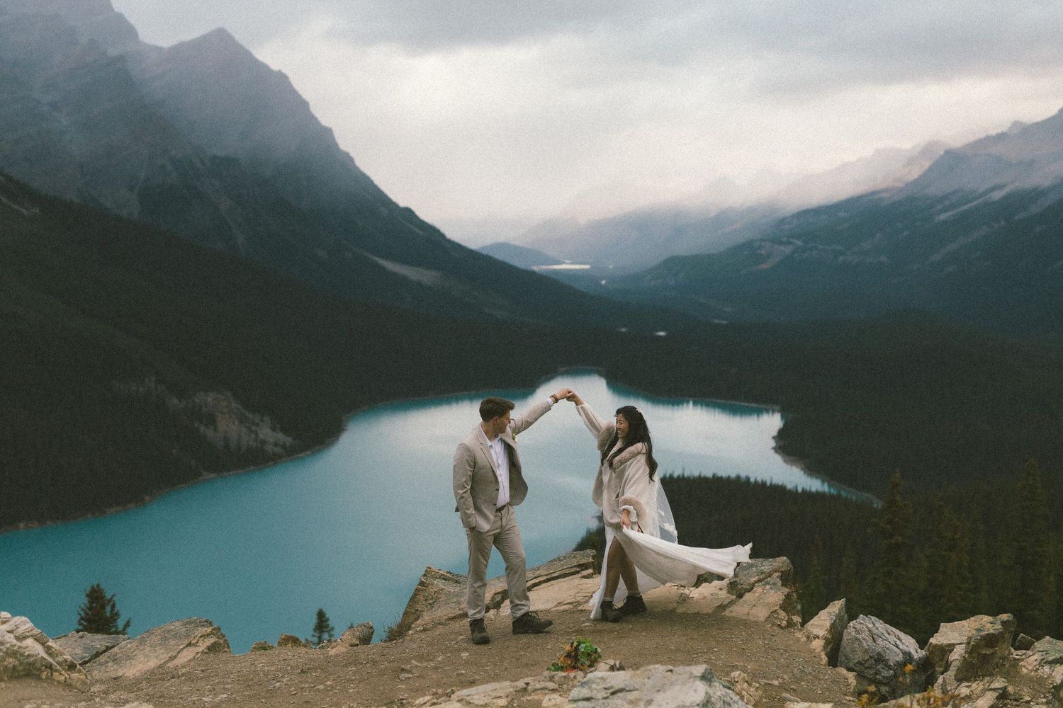 bride and groom twirl on a rocky outcrop above glacier-blue Peyto Lake in Banff