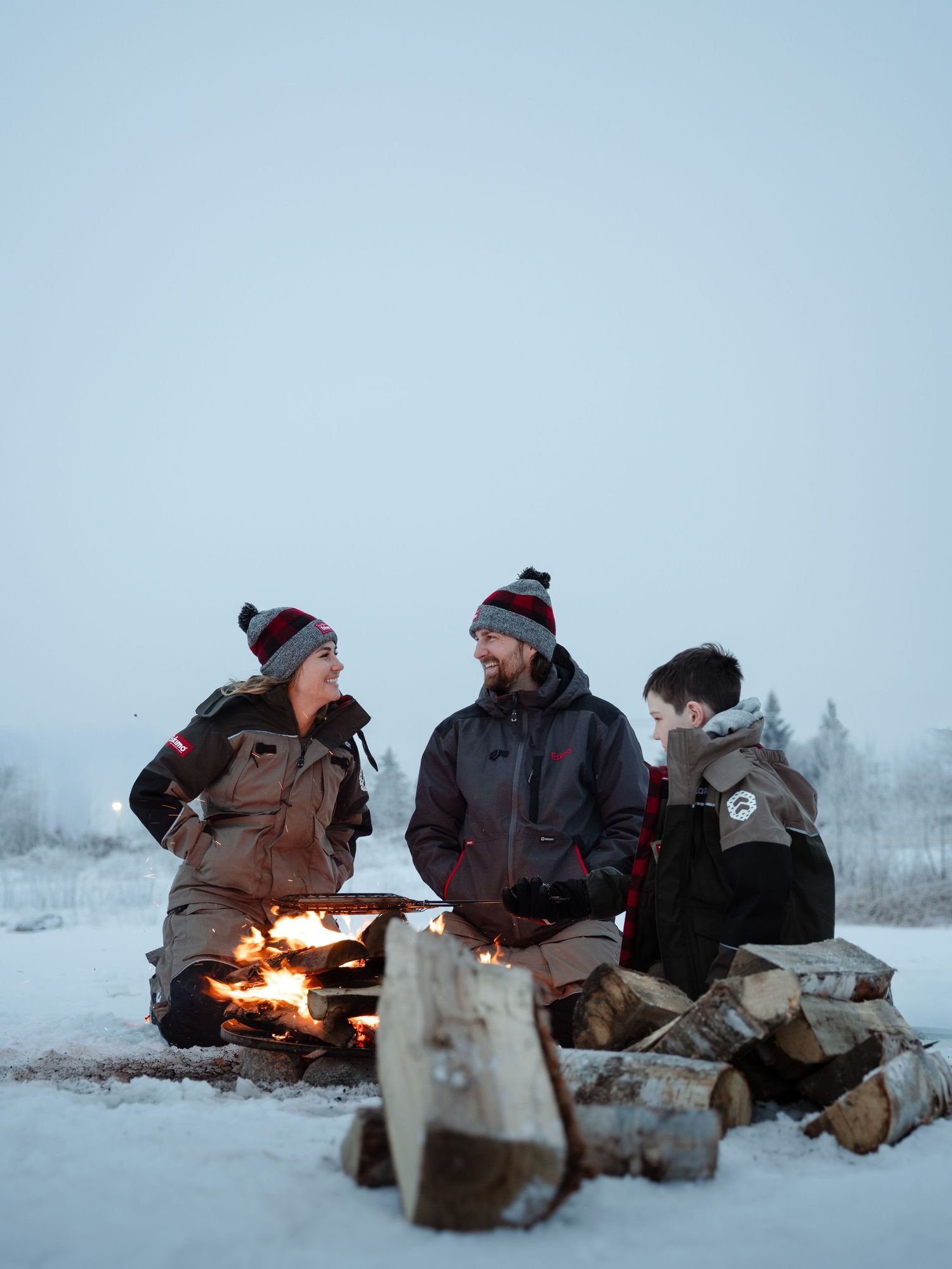 Group gathered around campfire on frozen lake during winter ice fishing adventure.