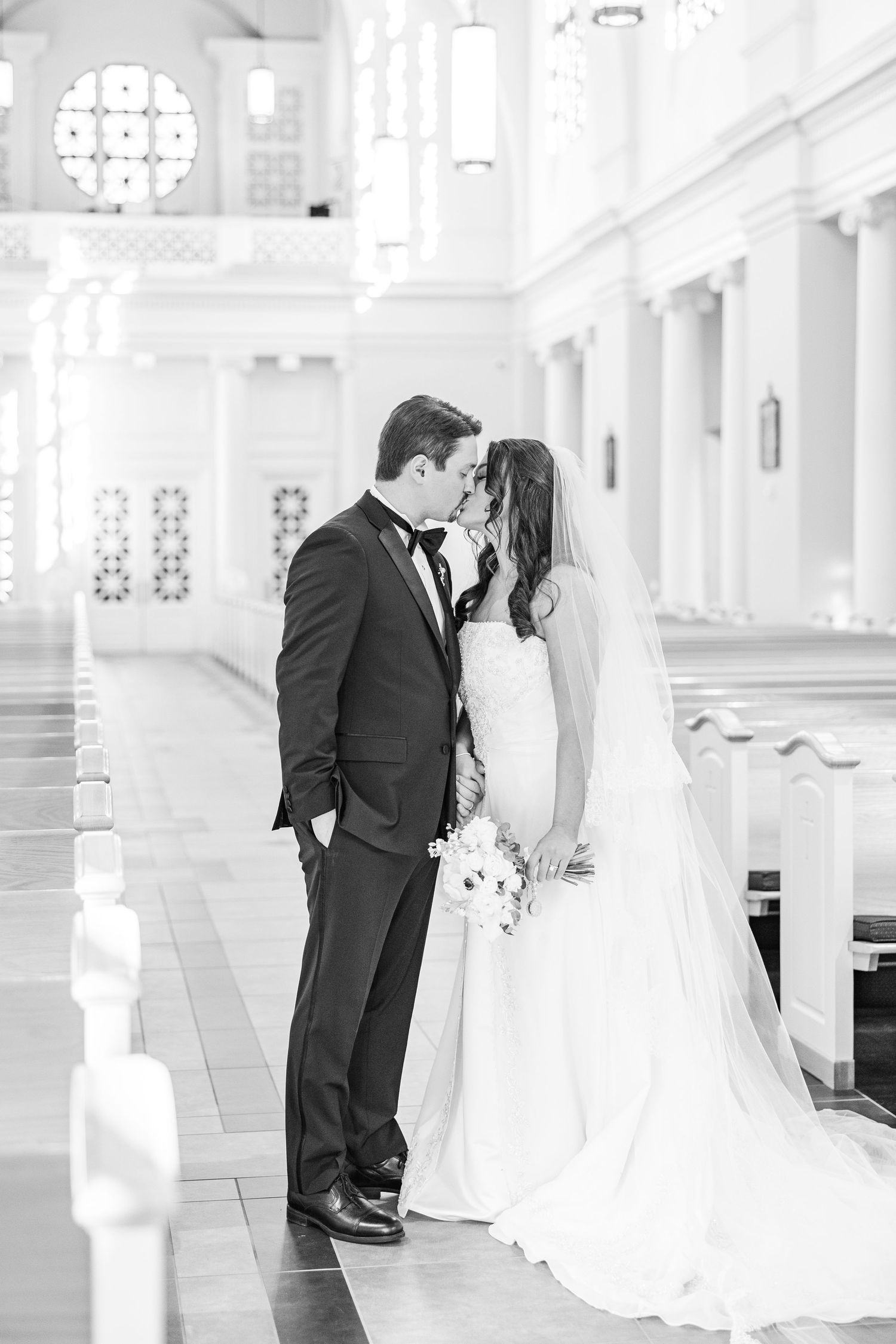 A romantic black and white wedding photo captured in an elegant church interior with white columns and natural light.