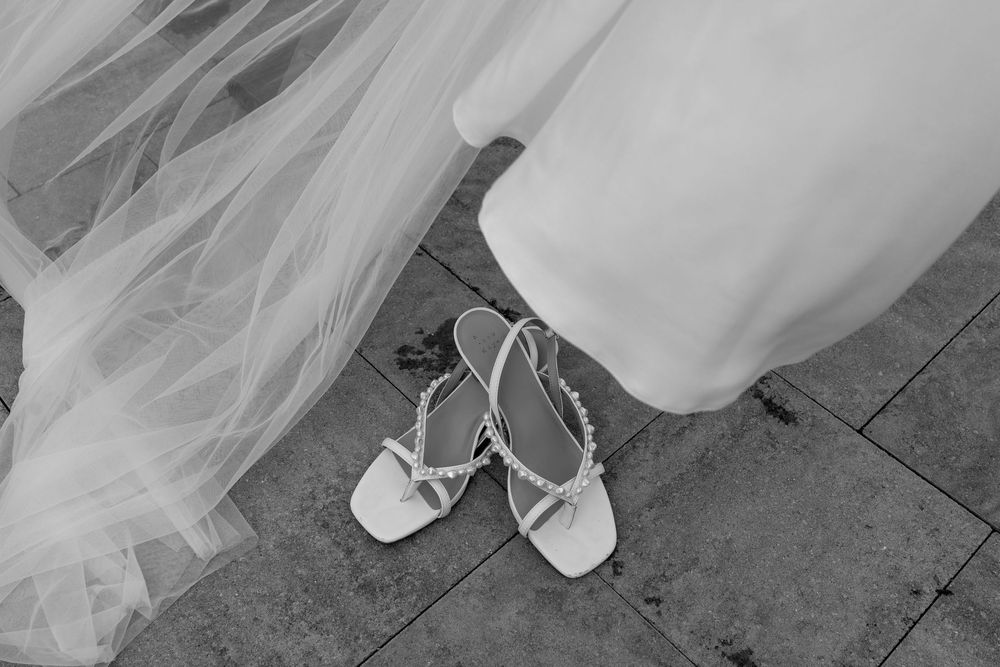 Black and white photo of bridal heels and veil on a stone floor.