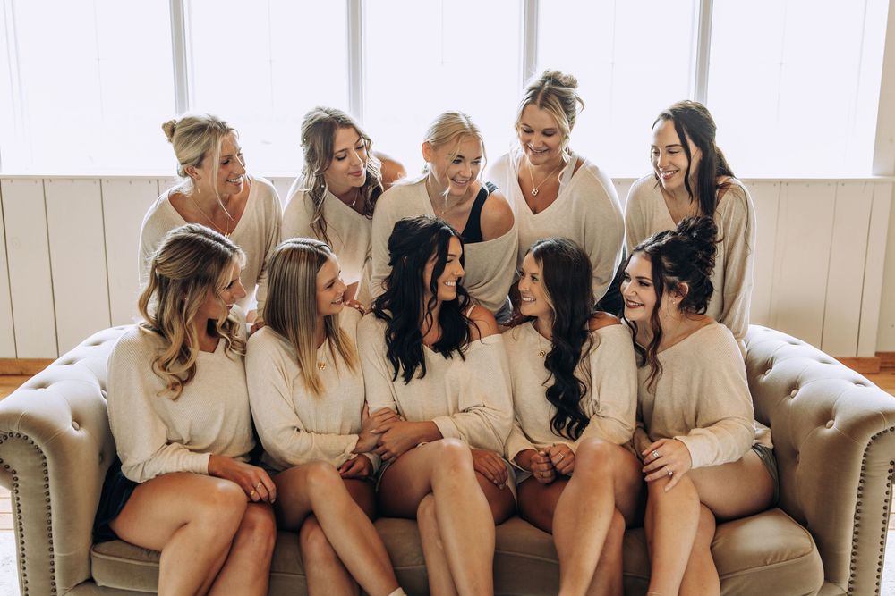 Group of bridesmaids in matching cream robes sitting and standing on a couch, smiling.
