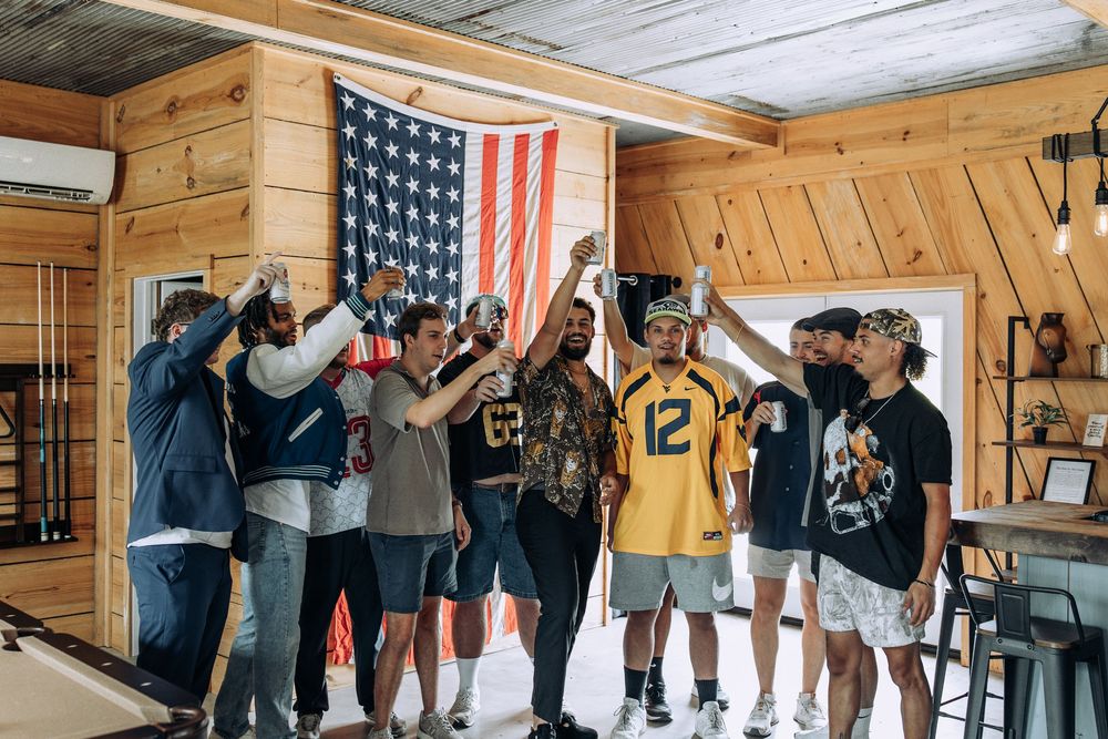 Groomsmen celebrating with raised hands in a rustic cabin room decorated with an American flag.