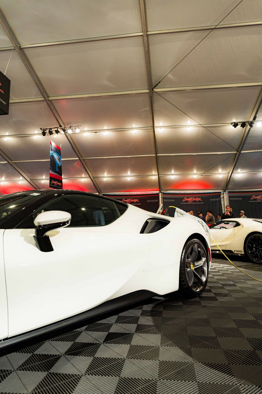 White supercars lined up in an indoor exhibition space featuring modern lighting and patterned floor tiles.