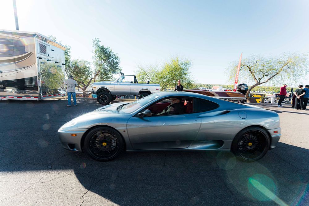 Panoramic view of luxury sports cars displayed at an indoor auto show with bright overhead lighting.