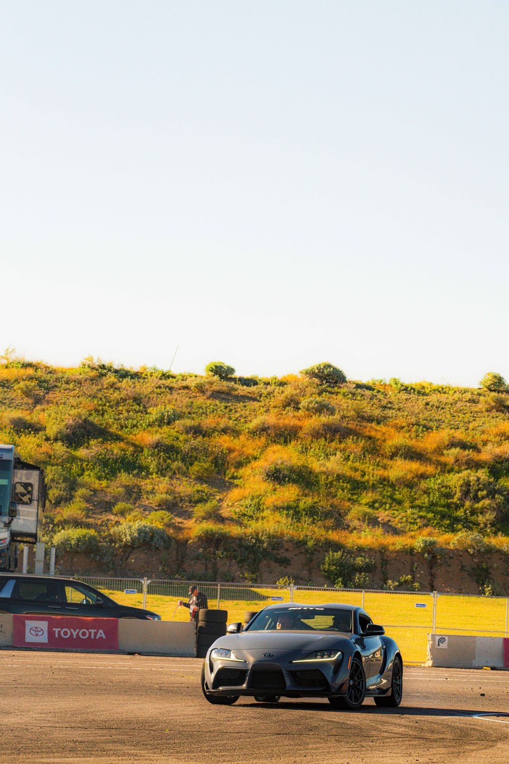 High-performance vehicles compete on a scenic racetrack surrounded by golden hills and desert landscape.