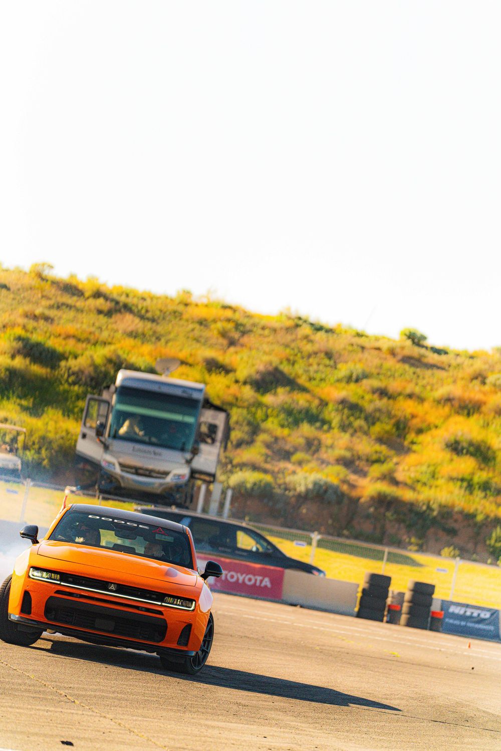 Sports cars racing on a desert track with yellow wildflowers and Toyota signage visible in the background.