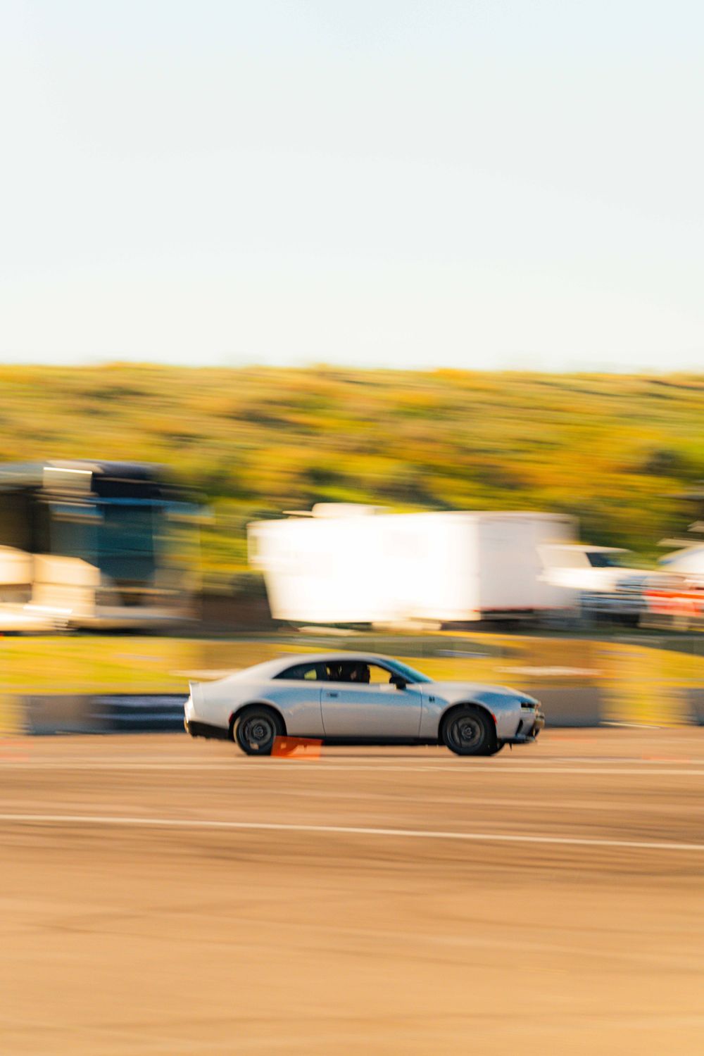 Silver sedan car racing on dirt track with motion blur effect during daytime competition.