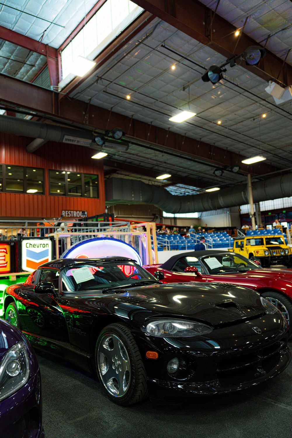 Classic muscle cars and sports cars lined up in indoor showroom with American memorabilia on display.