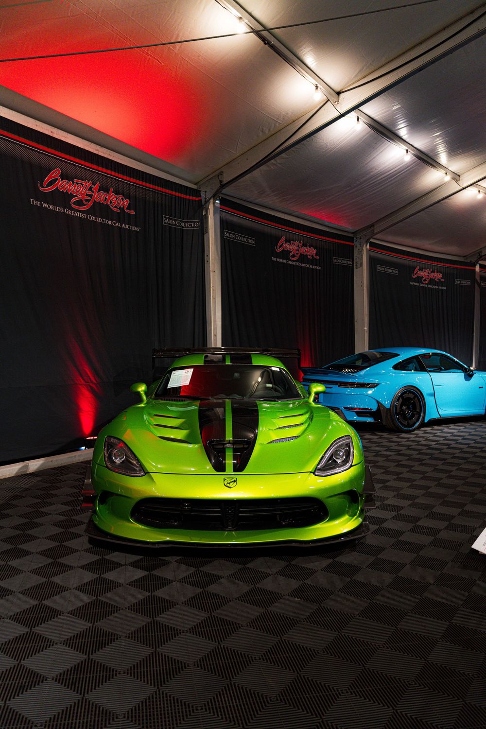 Lime green and blue sports cars on display in a dimly lit showroom with dramatic red accent lighting and checkered flooring.