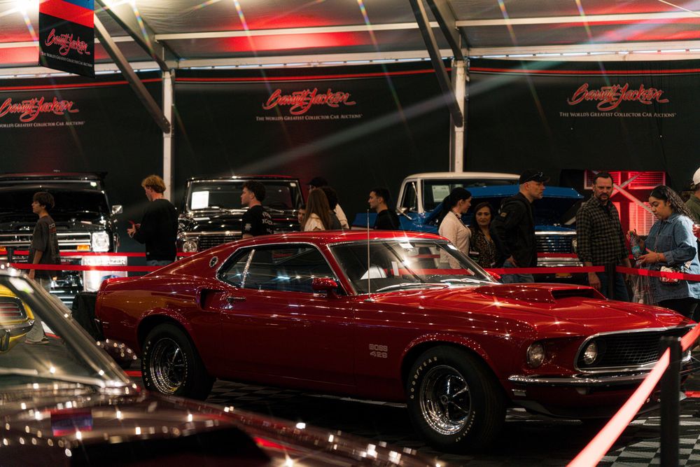 A classic red Ford Mustang Boss displayed under spotlights at an indoor car show.