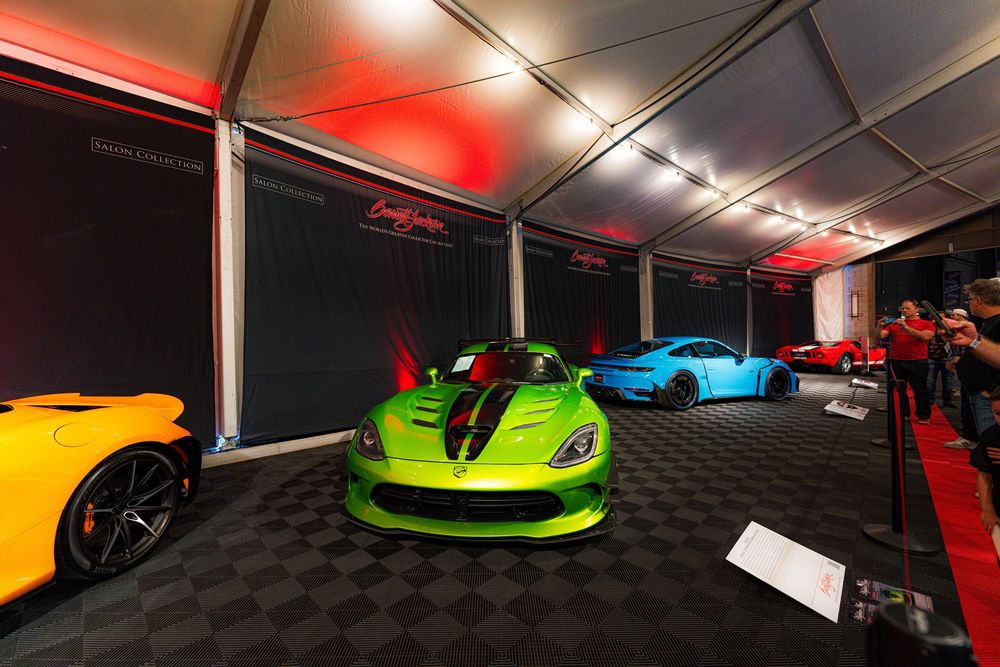 Exotic supercars including a bright green sports car displayed at an indoor auto show with red lighting.