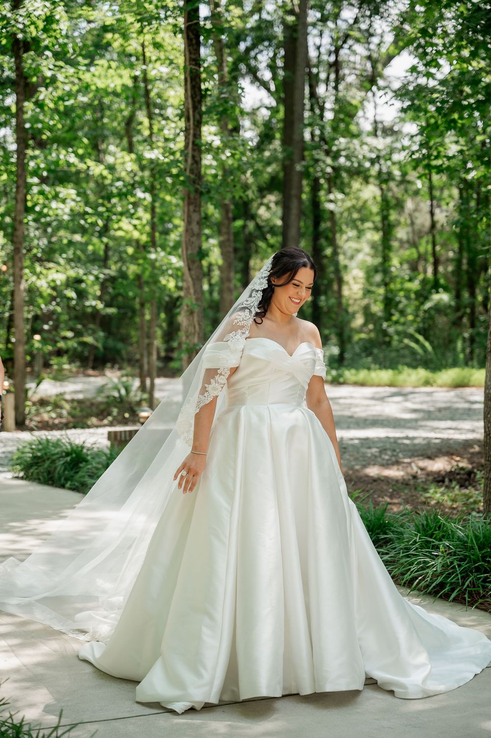 A bride in a ballgown style dress poses on a garden path surrounded by lush greenery.