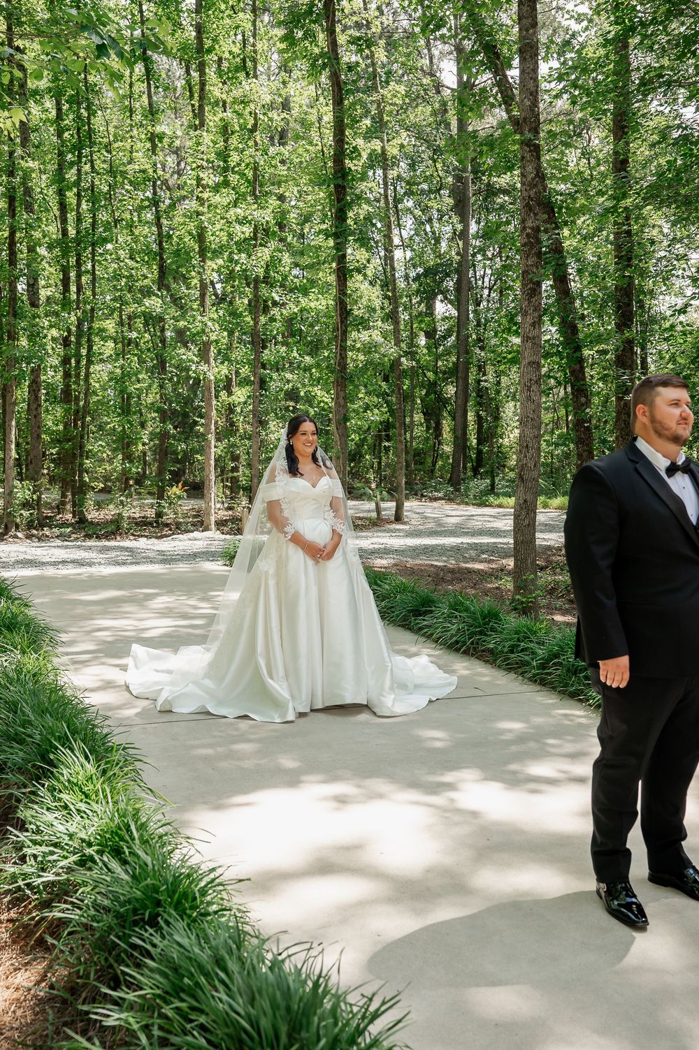 A wedding couple shares intimate moments on a tree-lined pathway during their first look.