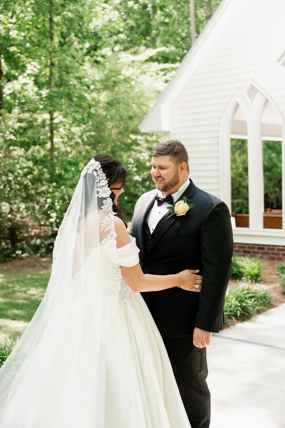 A romantic first look moment between newlyweds outside a white chapel building.