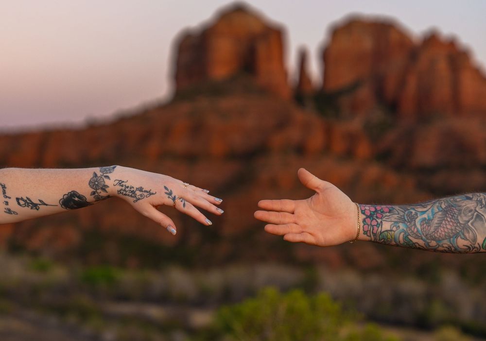 Tattooed hands reaching out against backdrop of red desert rock formations.