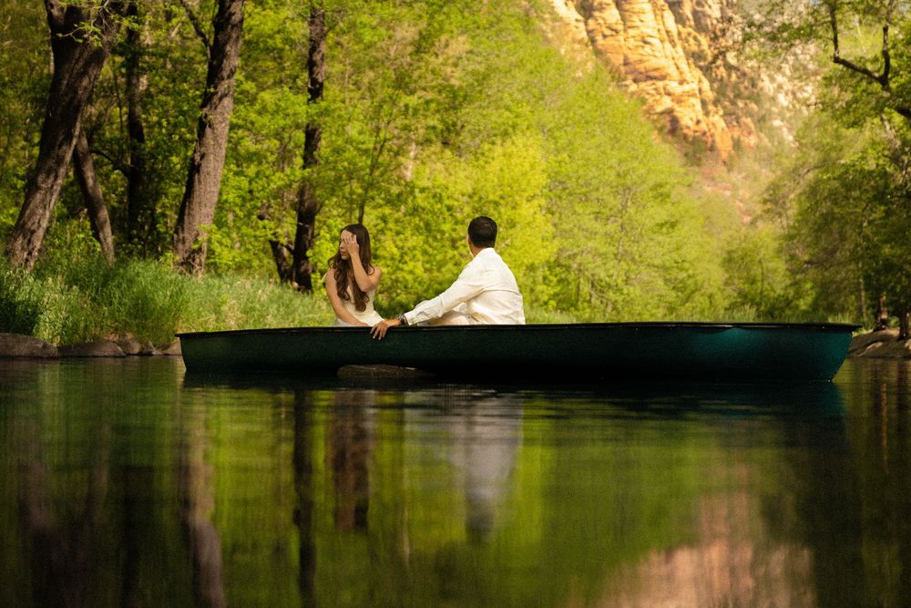 Romantic moment captured by lakeside with cliffs and greenery in background.