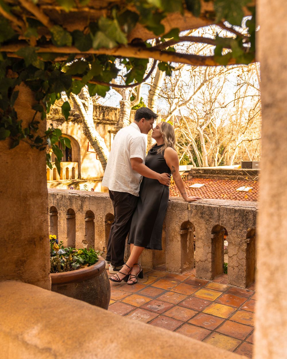 Couple sharing intimate moment on rustic terrace with Mediterranean architecture.