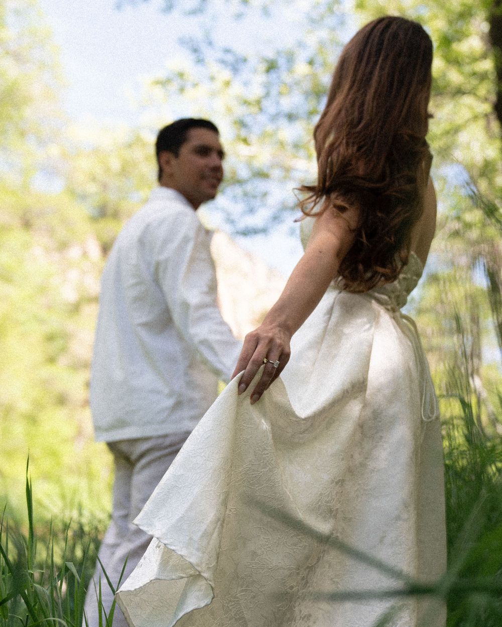 Couple in white clothing dancing through tall grass in soft natural light.