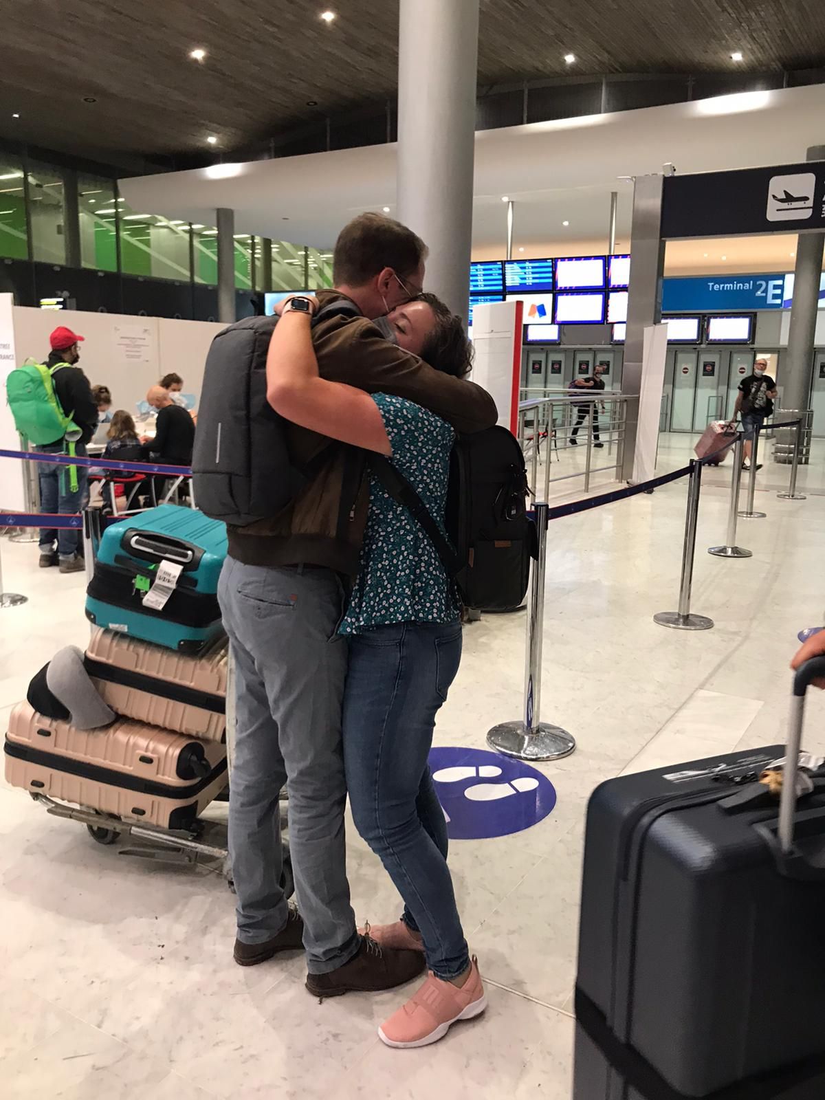 Emotional airport farewell embrace between two people with luggage and stanchions in the background.