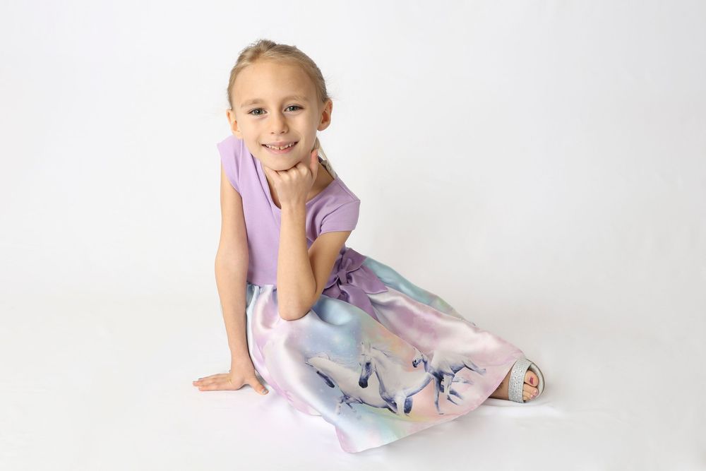 A dancer in a purple leotard and floral skirt performs graceful poses against a white backdrop.