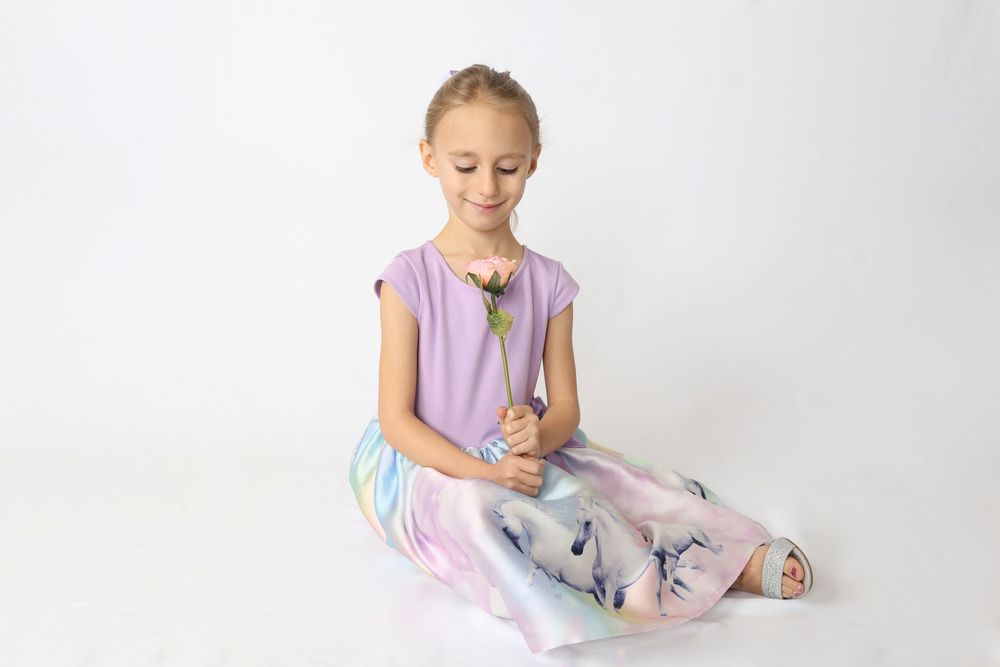 Young dancer in lavender leotard and tulle skirt practices ballet poses in a bright studio setting.