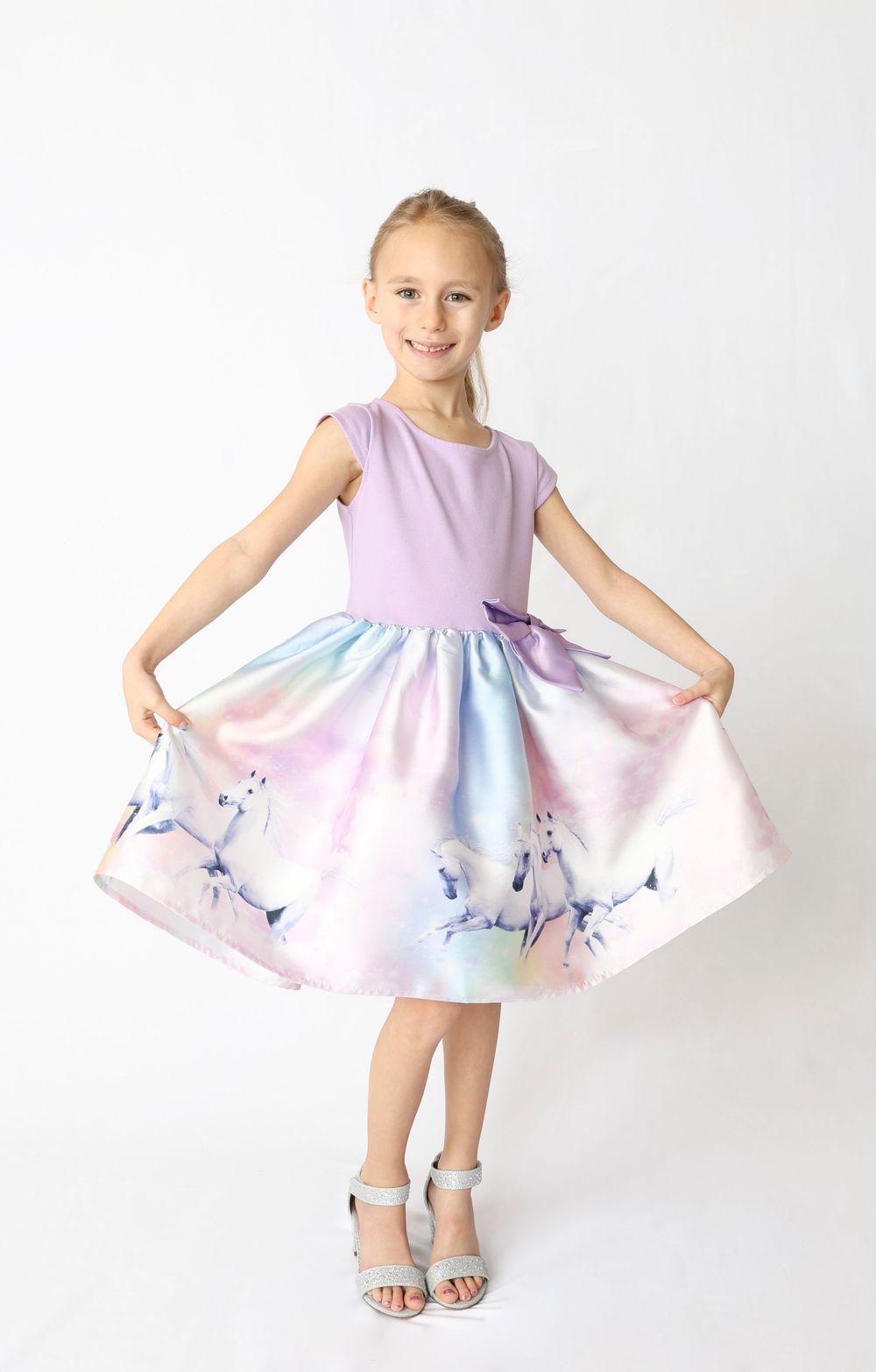 A child wearing a purple and white twirl dress with pastel watercolor patterns spins to show off the flowing skirt.