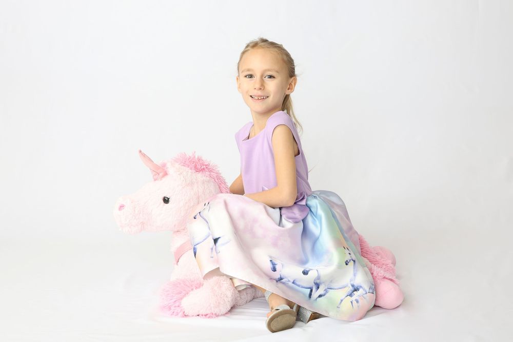 Child in pastel pajamas poses with plush unicorn toys against white backdrop.