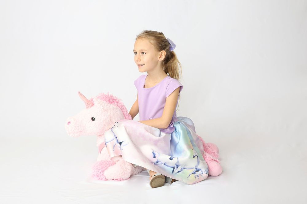 A person in pastel clothing poses with a pink stuffed unicorn plush toy against a white backdrop.