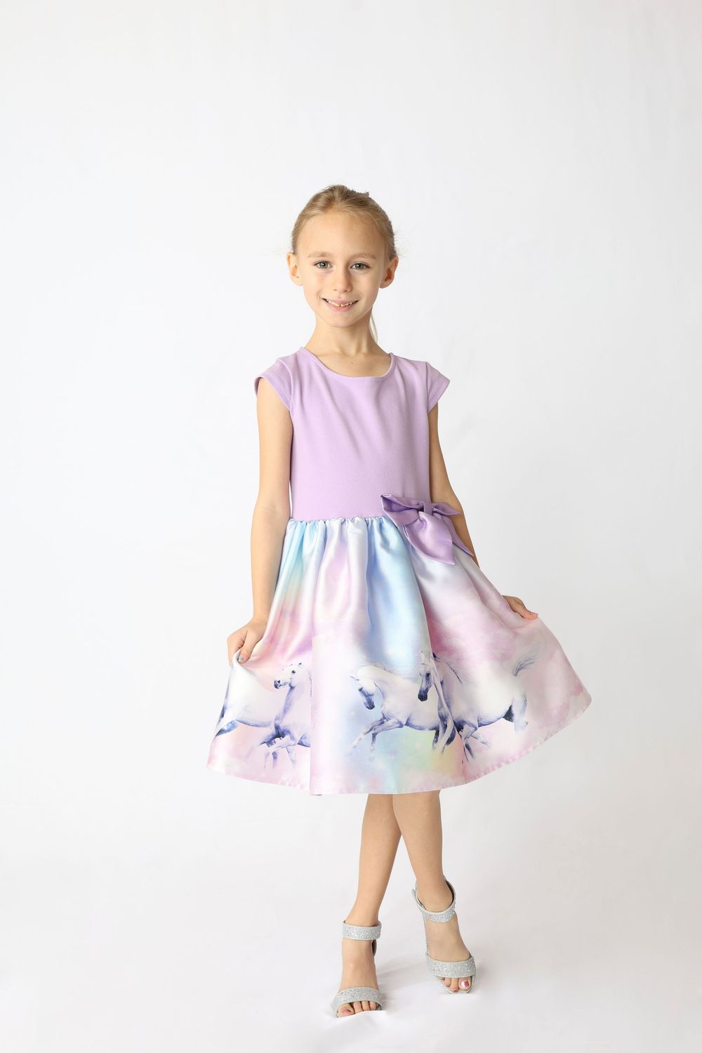 Young child wearing a pink and blue pastel dress with floral pattern twirls in front of white backdrop.