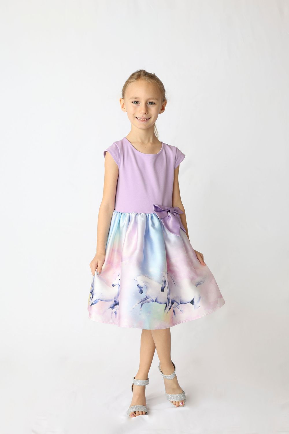 Toddler wearing a purple and blue floral dress poses in a studio setting against a white background.